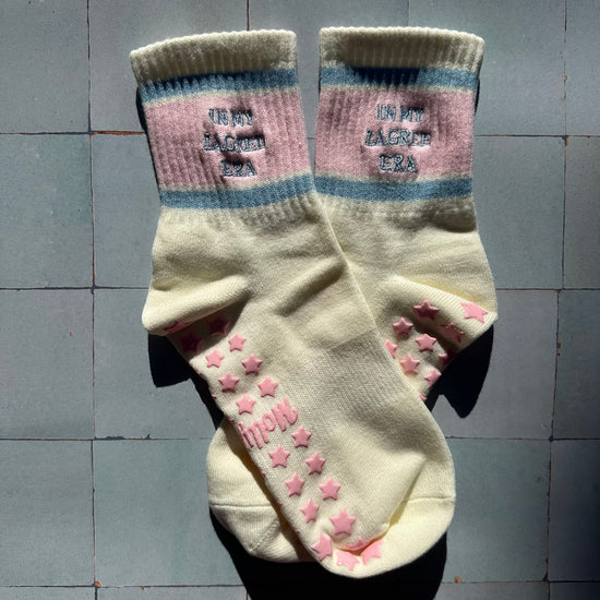 Cream pilates non slip grip sock with pink and blue stripes and pink star grips.  "in my lagree era" is embroidered on them. Used for Pilates, yoga, lagree and barre
