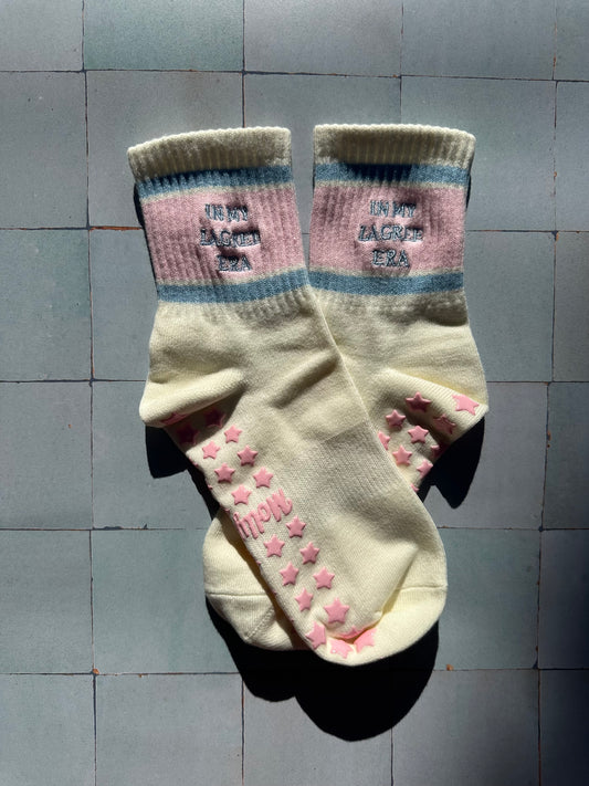 Cream pilates non slip grip sock with pink and blue stripes and pink star grips.  "in my lagree era" is embroidered on them. Used for Pilates, yoga, lagree and barre