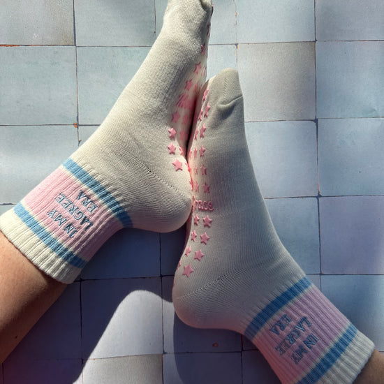 Cream pilates non slip grip sock with pink and blue stripes and pink star grips.  "in my lagree era" is embroidered on them. Used for Pilates, yoga, lagree and barre